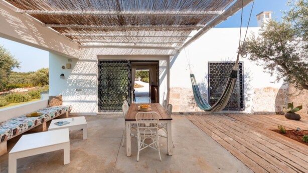 Un patio al aire libre con una mesa y sillas de madera, un banco acolchado y una hamaca.