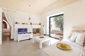 Een moderne woonkamer met een flatscreen televisie, een witte salontafel, een bank en een groot raam met uitzicht op de omgeving.