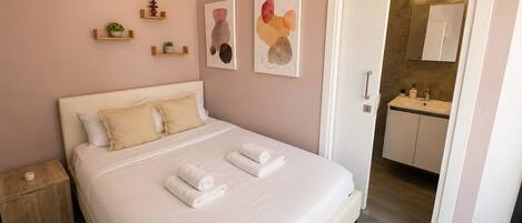 Una habitación de hotel con cama, mesita de noche y baño visible a través de una puerta abierta.