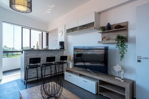 A modern kitchen with a large TV, bar stools, and a dining table.
