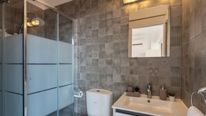 Ein modernes Badezimmer mit Duschkabine aus Glas, Toilette, Waschbecken mit Spiegel und einem Handtuch an der Wand.