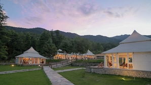 A series of white tents with glass walls, set on a stone-paved path, surrounded by lush greenery and mountains in the background. - Tenzinling Luxury Villa Tent (Paro)