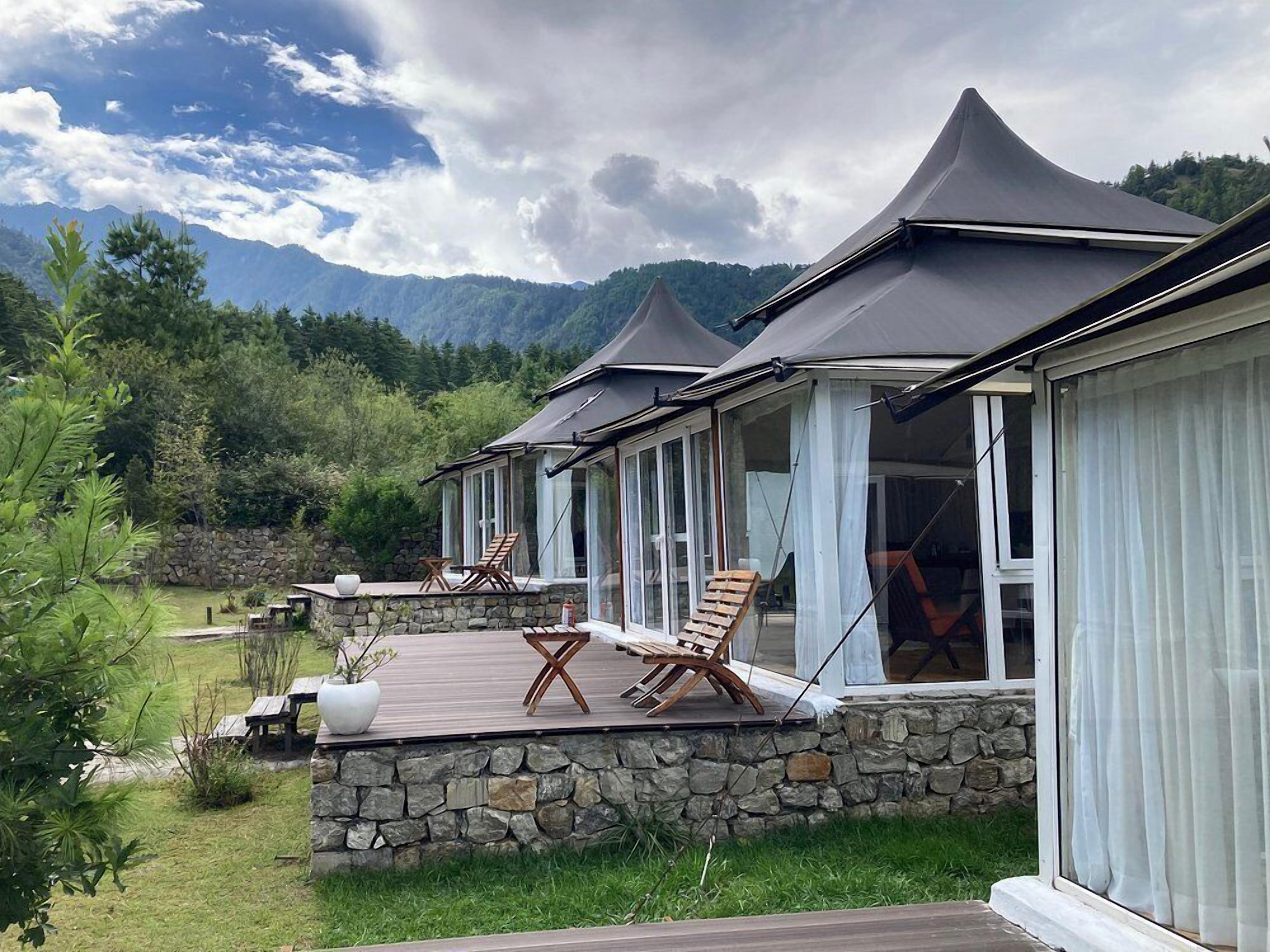 A row of modern, single-story cabins with large windows and a stone foundation, set in a lush, mountainous landscape.