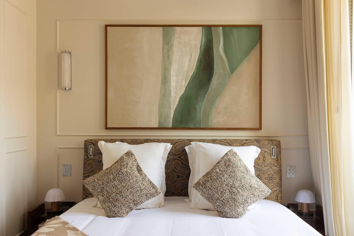 Ein Hotelzimmer mit einem großen Bett, zwei Zierkissen, einem Wandbild und einem Nachttisch mit einer Lampe.