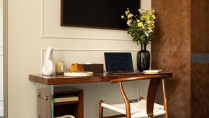 Een moderne kantoorruimte met een bureau, stoel, laptop, vaas met bloemen en een grote flatscreen aan de muur.