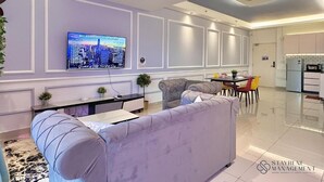 A modern living room with a grey sofa, a flat-screen TV mounted on the wall, and a dining area with a table and chairs. - Meridin Medini SOVO by Stayrene (Iskandar Puteri)