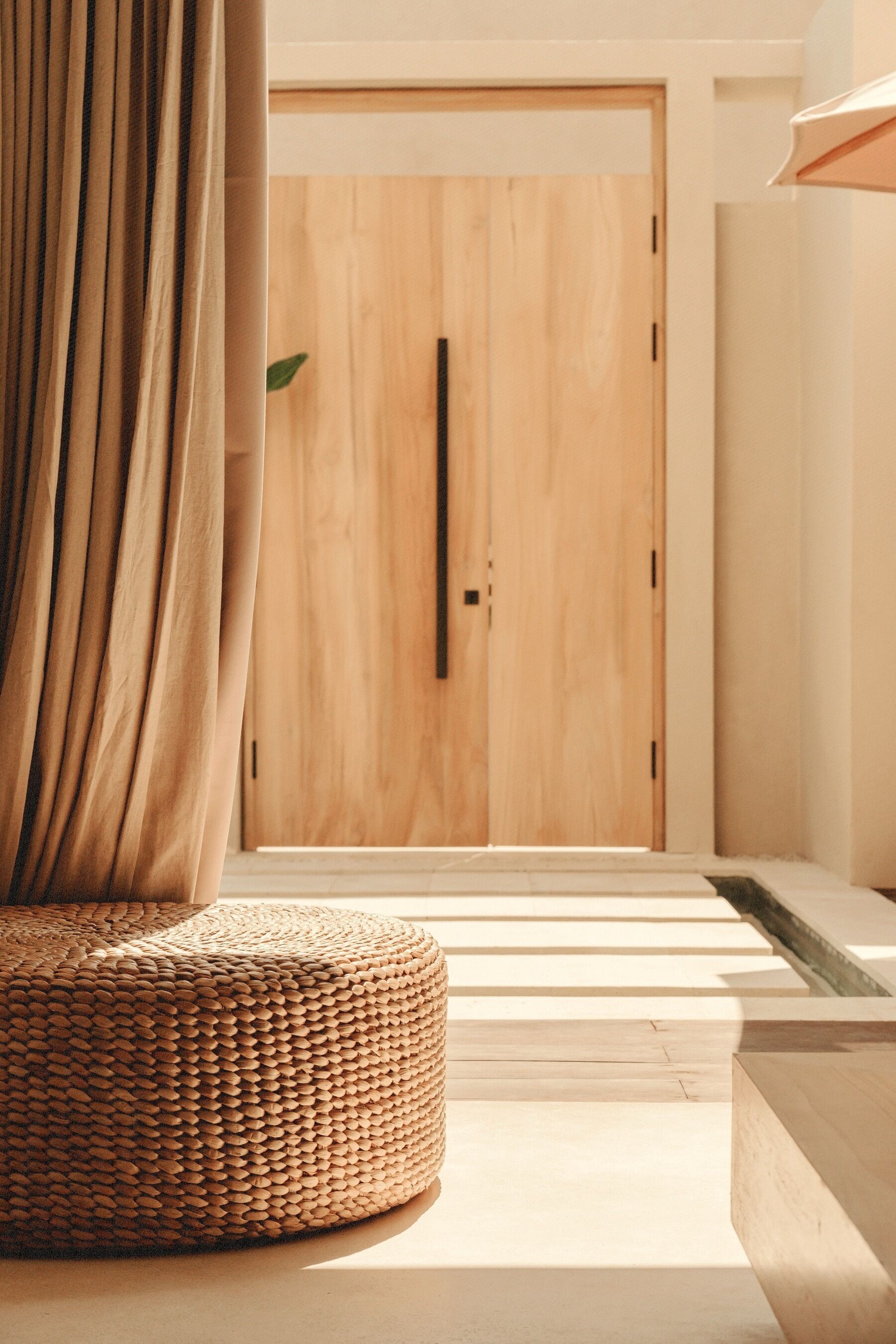 Un interno moderno con una porta in legno, un poggiapiedi intrecciato e un design minimalista.