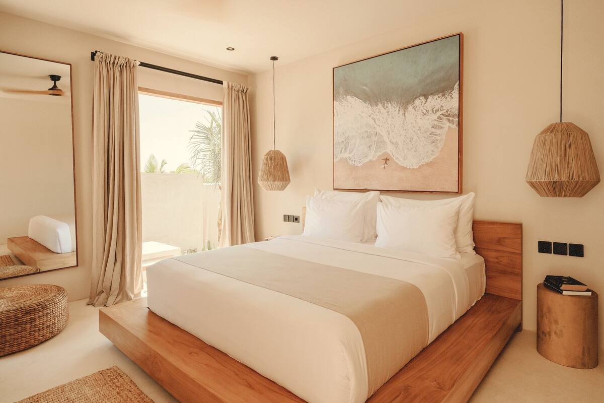 Ein modernes Schlafzimmer mit einem großen Bett, einer Holzplattform, einer Hängeleuchte und einem Strandbild.