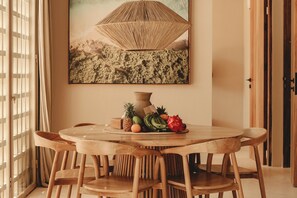 A round wooden table with chairs, a woven light fixture, and a fruit arrangement on the table. - Nori Boutique Villas (Pecatu)
