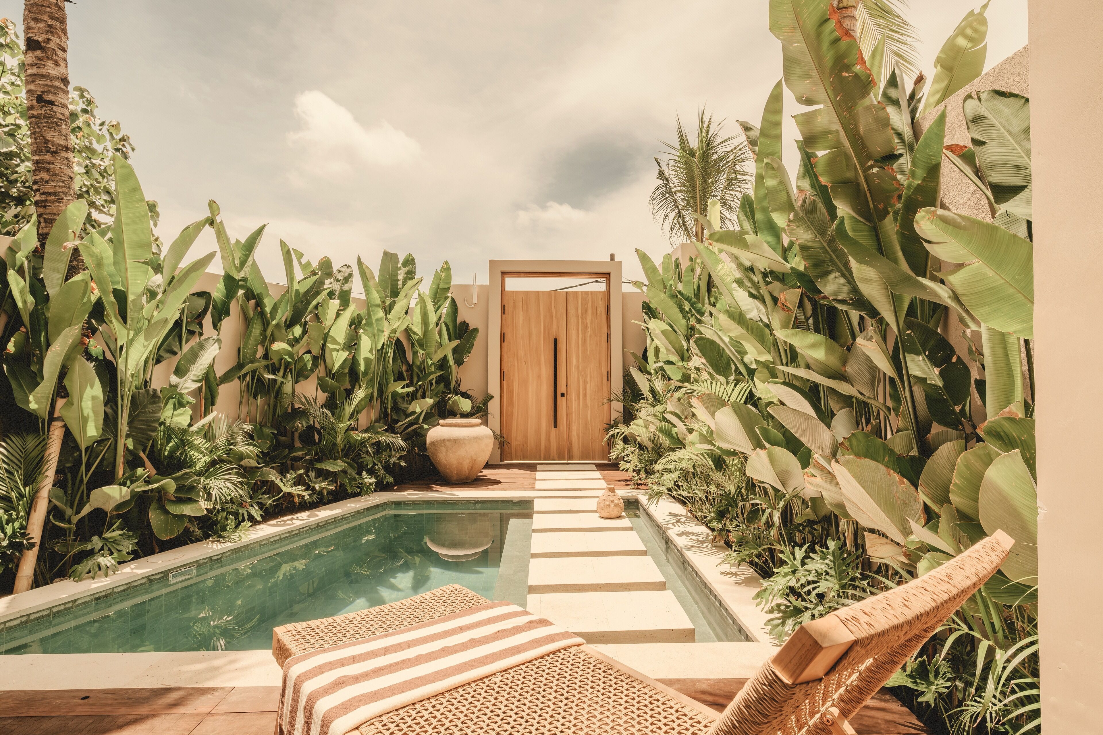 A pool area with a wooden door, surrounded by lush tropical plants.