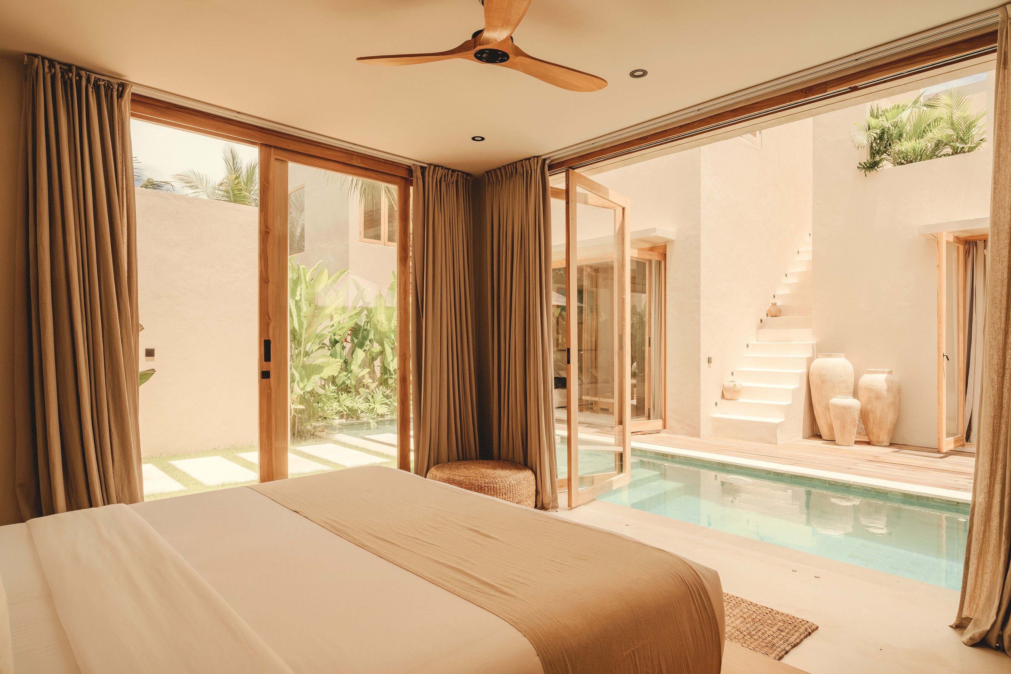 A bedroom with a large bed, a ceiling fan, and a view of an outdoor swimming pool.