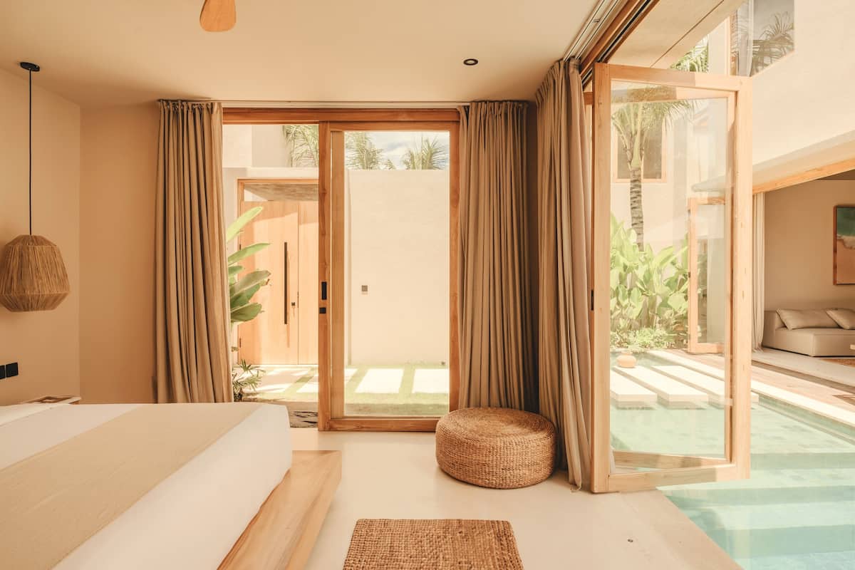 Ein modernes Schlafzimmer mit einem großen Bett, einer kleinen, runden Sitzecke und einer Glastür, die zu einem Poolbereich führt.