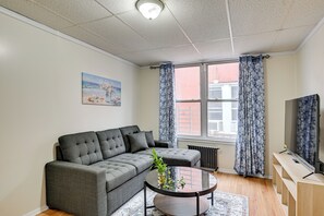 Ein modernes Wohnzimmer mit einem grauen Ecksofa, einem Glastisch und einer Holz-TV-Konsole.