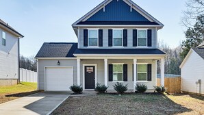 Una casa a due piani con tetto blu scuro, rivestimento bianco e un garage anteriore.