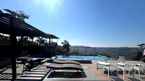 Un espace extérieur avec piscine, des chaises longues et un coin salon abrité, le tout agrémenté d’un cadre pittoresque.