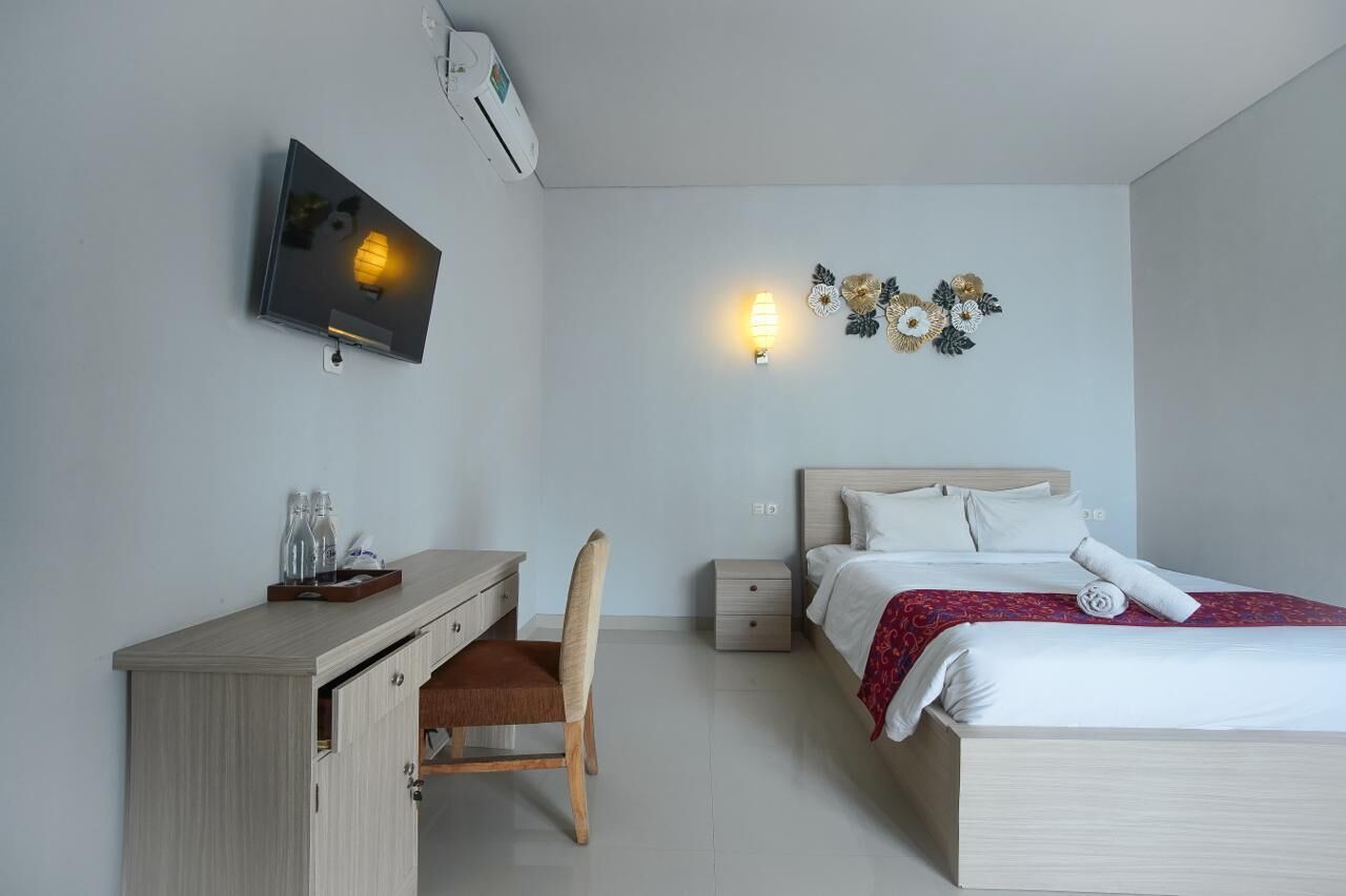 Habitación de hotel con cama, escritorio, silla, televisor, lámpara de pared y un adorno mural.