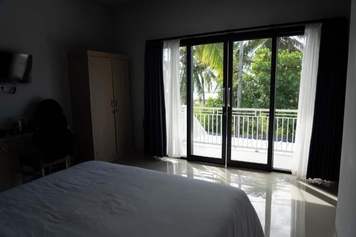 A hotel room with a bed, a wardrobe, and a sliding glass door to a balcony with a view of greenery.