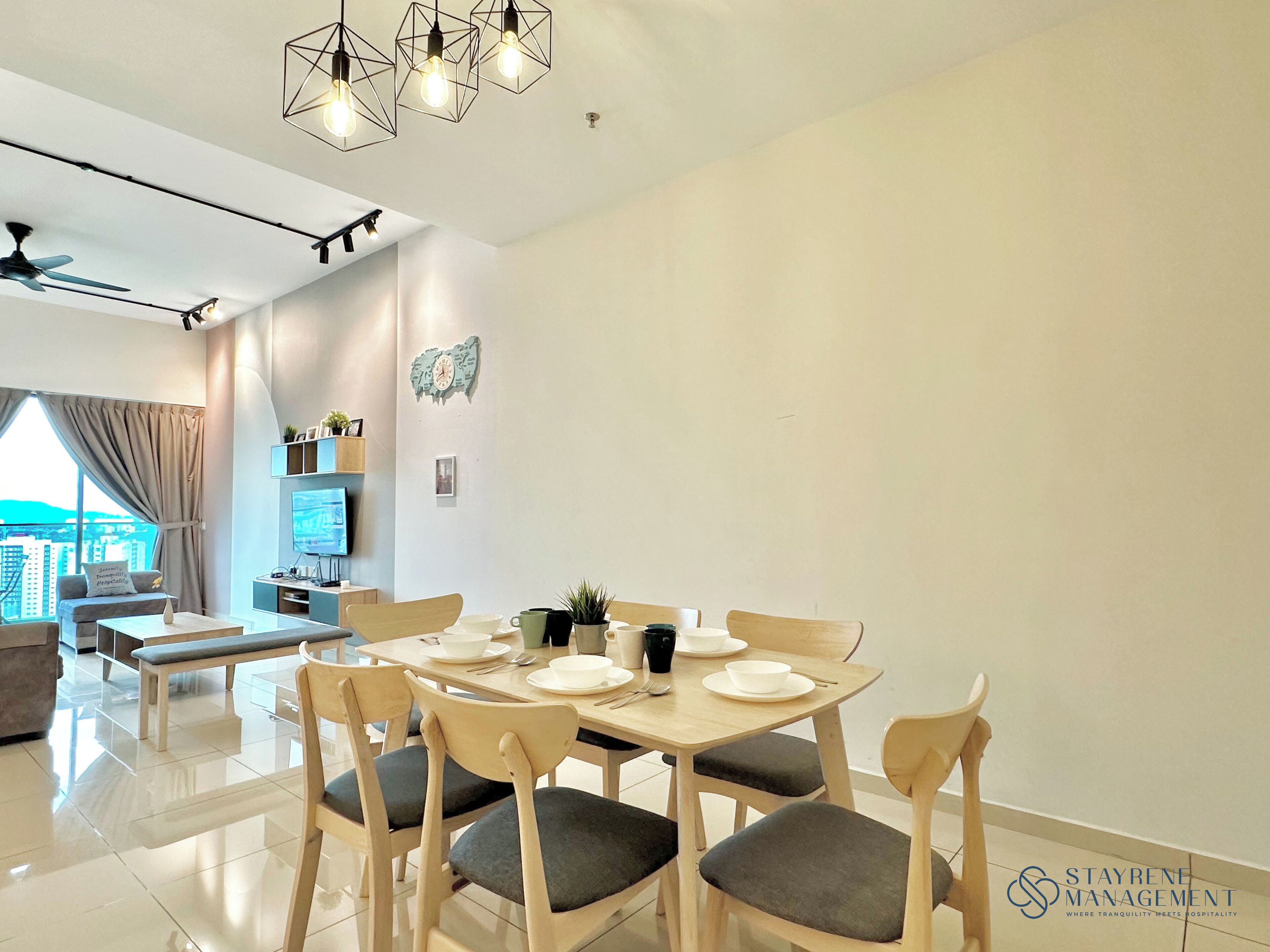 A modern dining area with a wooden table set for four, surrounded by cushioned chairs. A television is mounted on the wall, and a cityscape is visible through the window.
