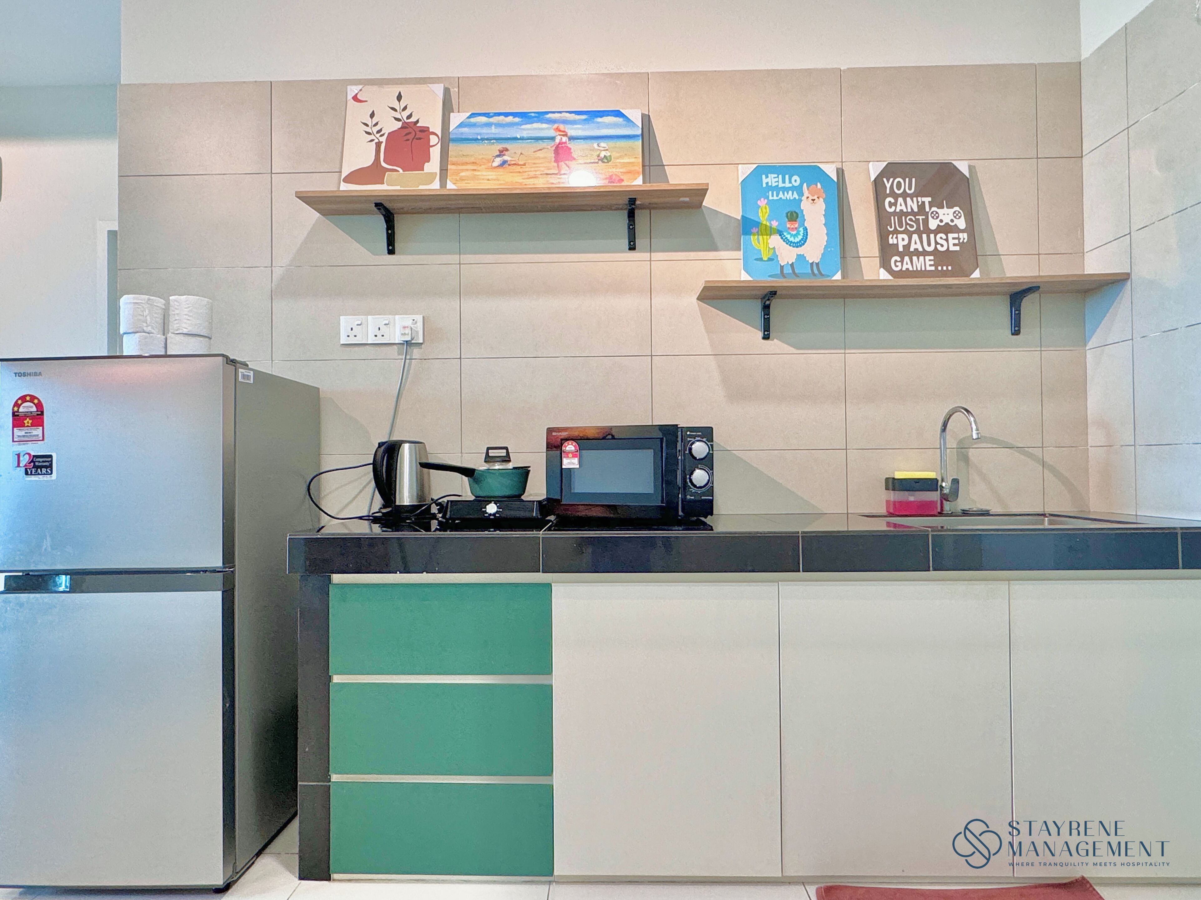 A kitchen with a refrigerator, microwave, stove, and a shelf with artwork.