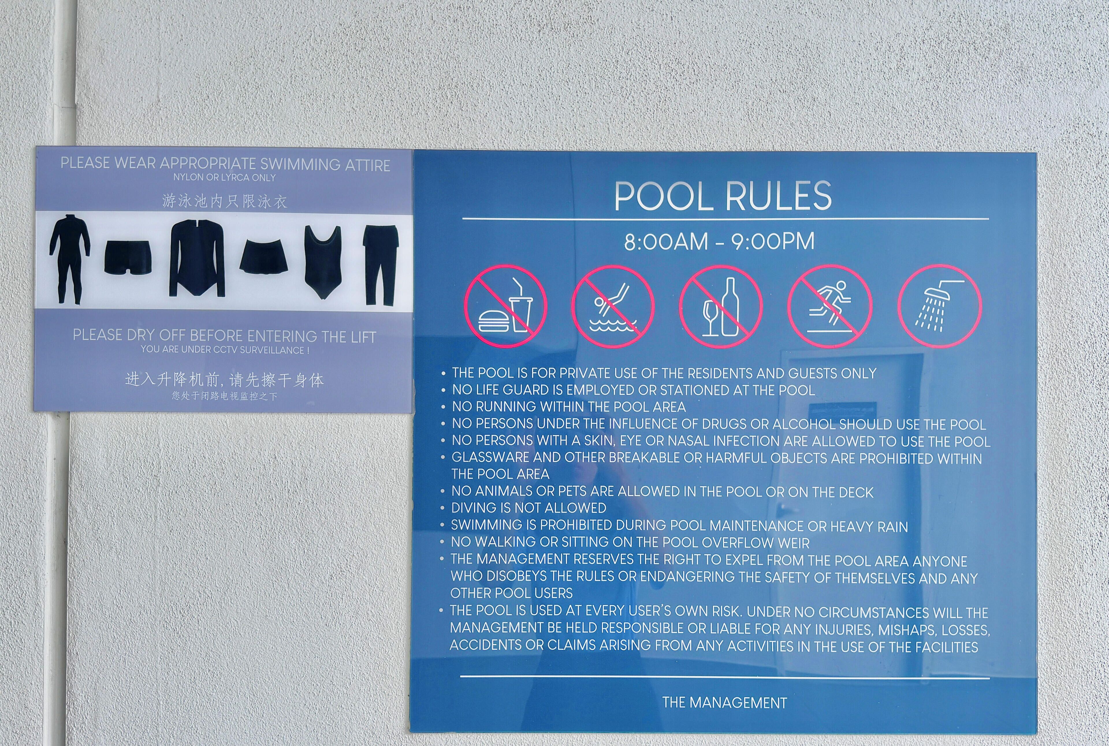 A pool rules sign with prohibited activities and a sign advising to wear appropriate swimming attire.