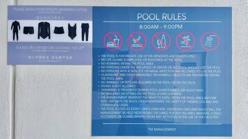 A pool rules sign with prohibited activities and a sign advising to wear appropriate swimming attire.
