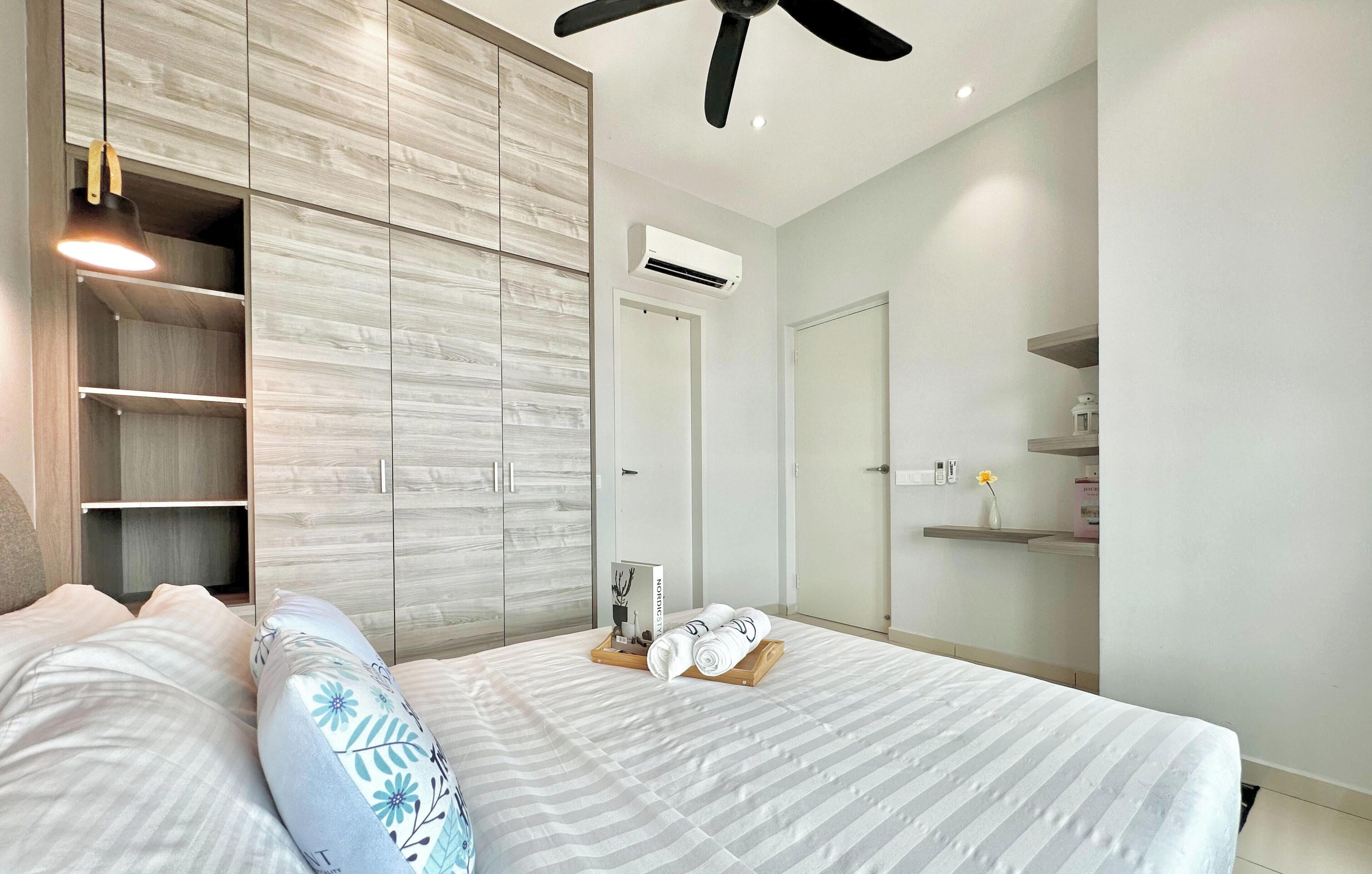A bedroom with a bed, a wardrobe, a ceiling fan, and a bedside table with a book and a tray.