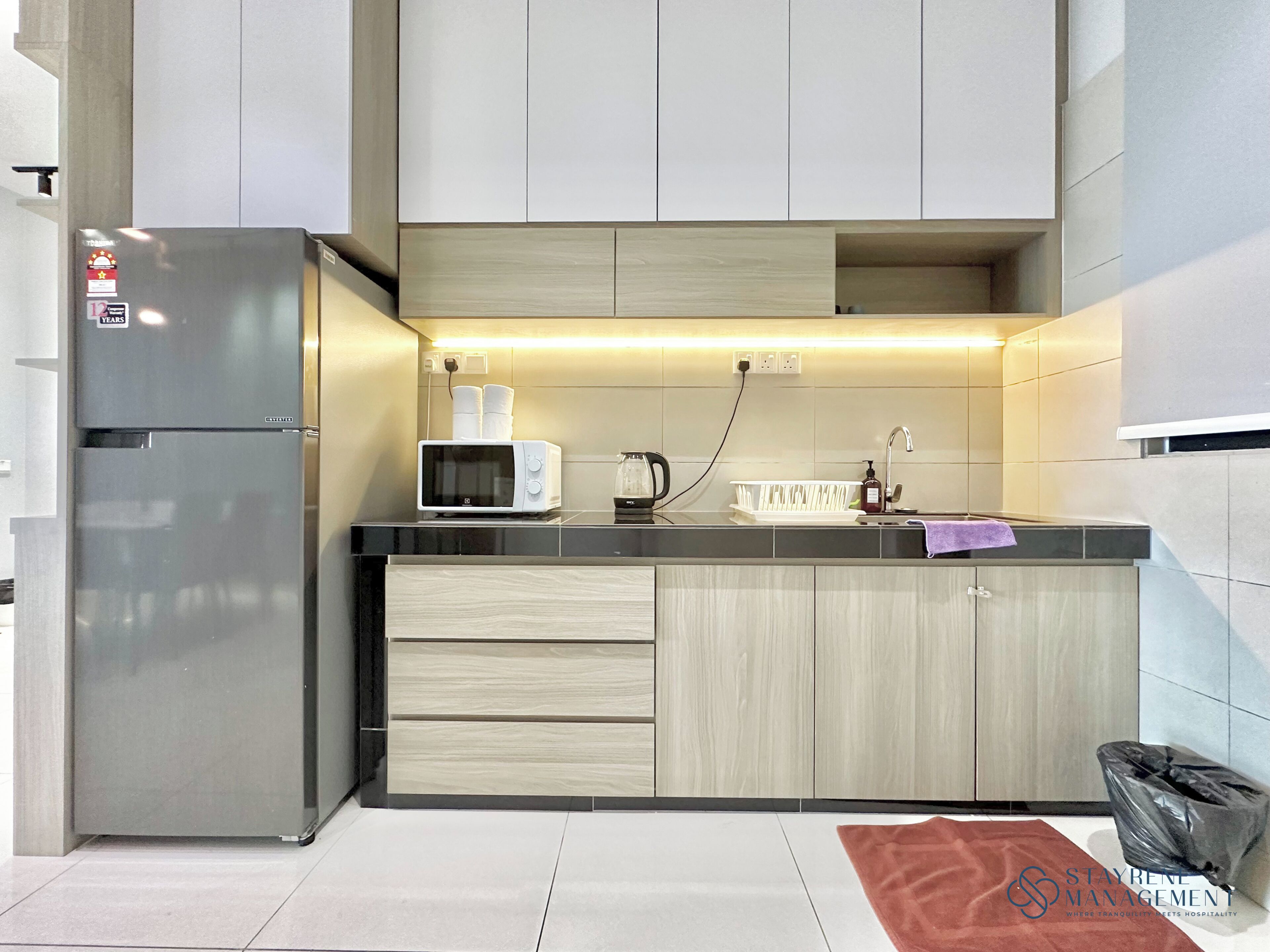 A modern kitchen with a built-in refrigerator, microwave, and kettle.