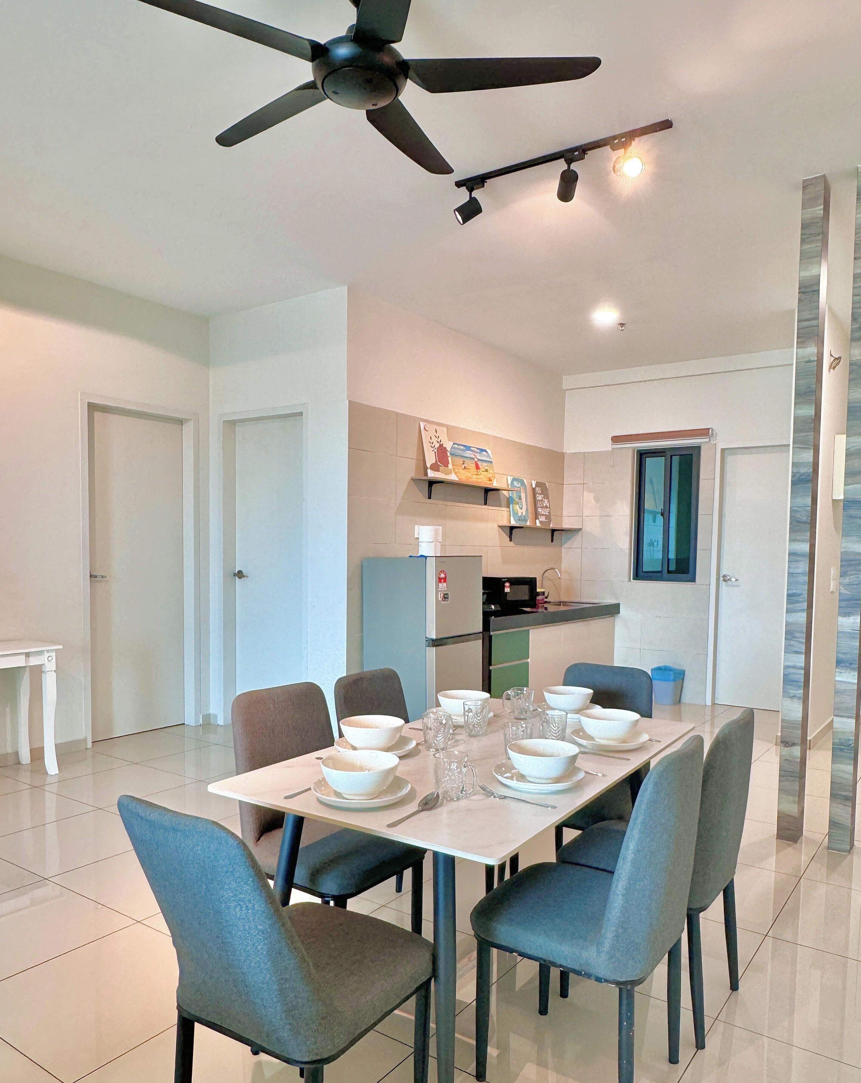 A dining area with a table set for six, chairs, a ceiling fan, and a kitchen in the background.