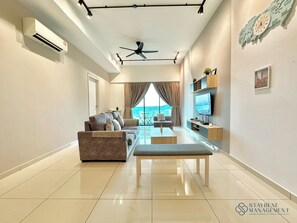 A modern living room with a sofa, a coffee table, and a TV. There is a ceiling fan, a wall-mounted TV, and a window with curtains. - Melaka Ong Kim Wee Residence by Stayrene (Malacca City)
