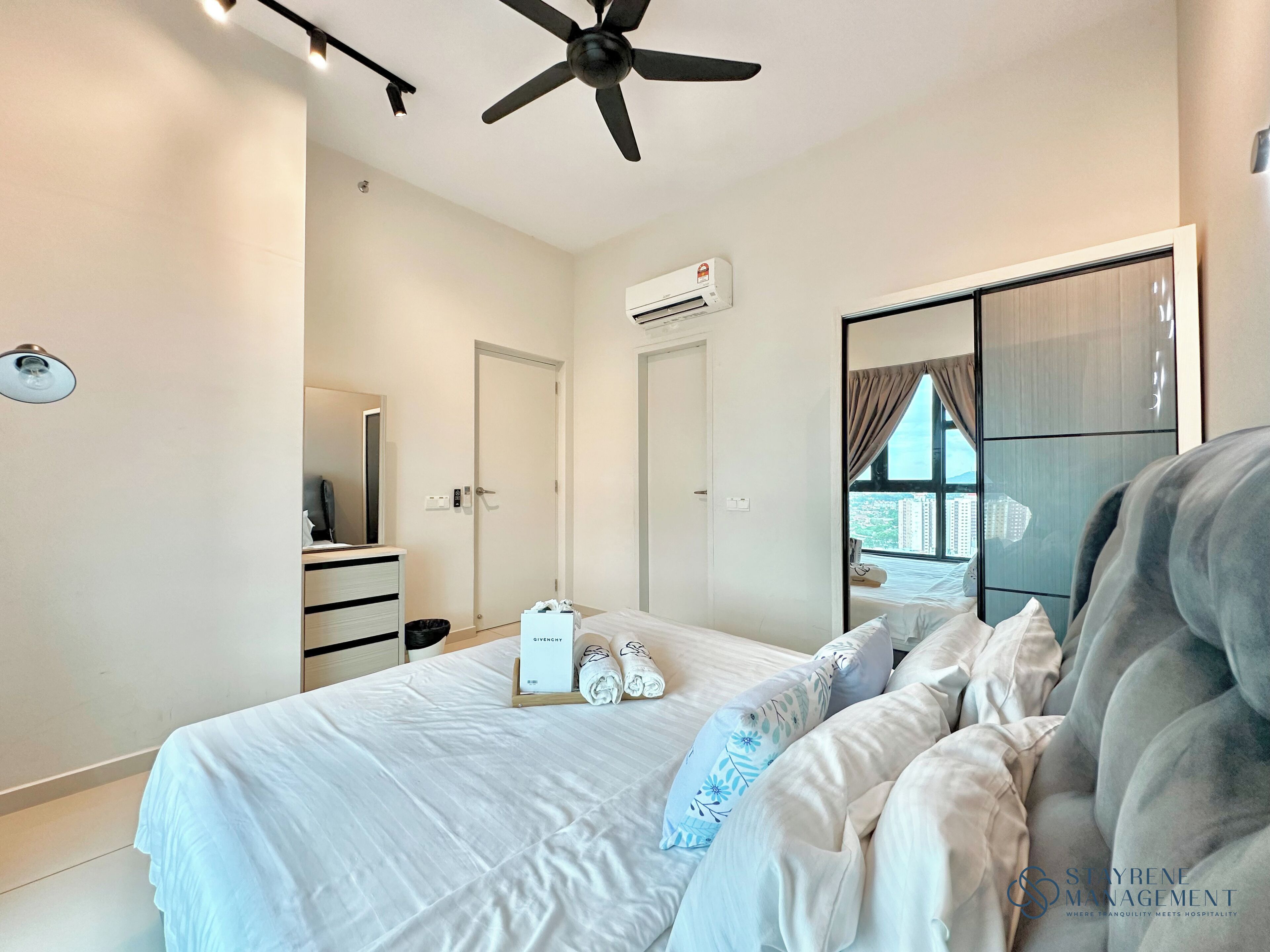 Une chambre d’hôtel moderne équipée d’un lit, d’un ventilateur de plafond, d’un climatiseur, d’une armoire et offrant une vue sur la ville par une fenêtre.