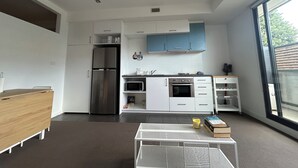 Eine moderne Küche mit weißen und blauen Schränken, einem Edelstahl-Kühlschrank, einer Mikrowelle und einem Gasherd. Es gibt eine kleine Essecke mit einem weißen Tisch und Stühlen.