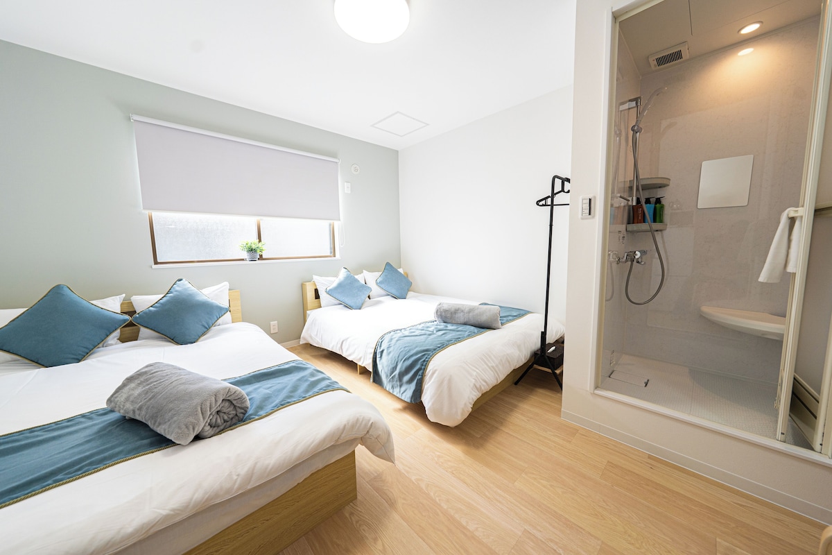 A hotel room with two beds, a shower area, and a window with blinds.