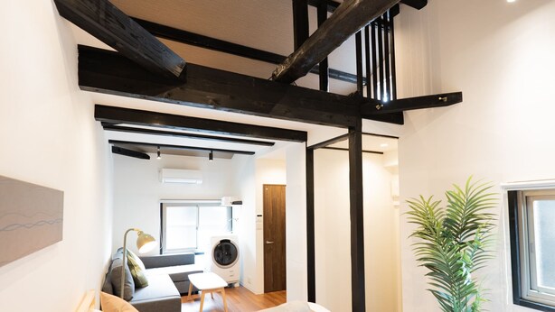 A modern bedroom with two beds, wooden beams, a potted plant, and a view of the living area. - JP RESERVE Tenshitsukinuke (Kyoto)