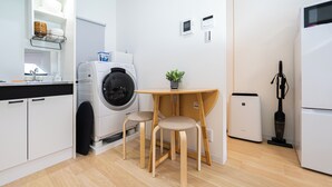 A compact kitchen with a washing machine, a small table with two chairs, and a compact refrigerator. - JP RESERVE Tenshitsukinuke (Kyoto)