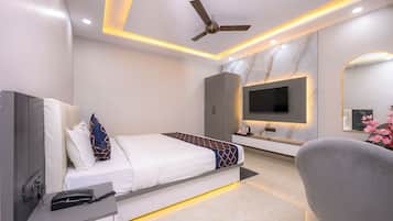 Quarto de hotel moderno com cama, escrivaninha, cadeira, televisão e ventoinha no teto.