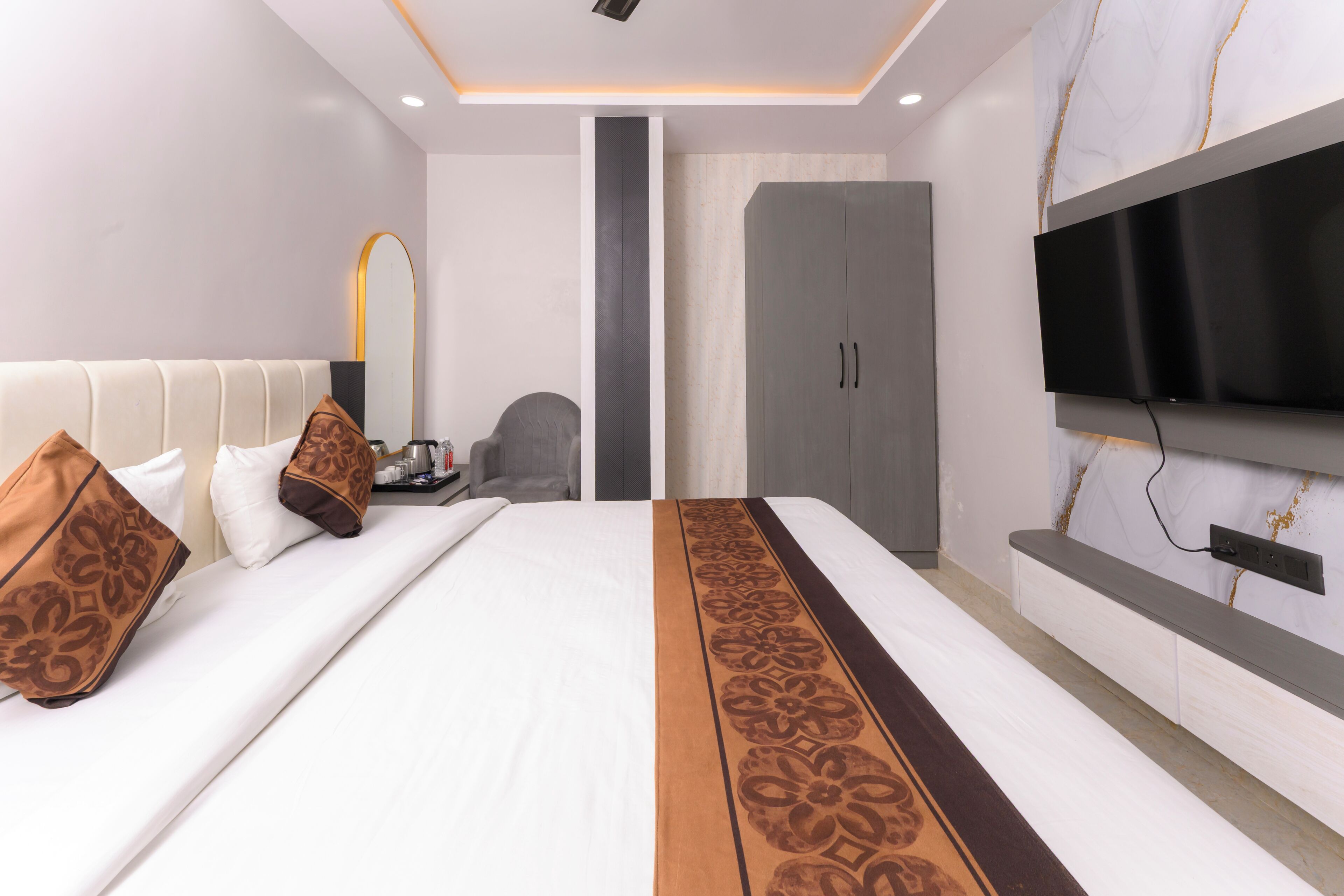 A modern hotel room with a large bed, a flat-screen TV mounted on the wall, a wardrobe, and a seating area with a chair.