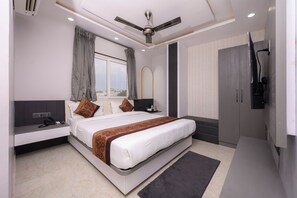 A modern hotel room with a large bed, a seating area, a wardrobe, and a ceiling fan. - Hotel Maharani Palace (varanasi)