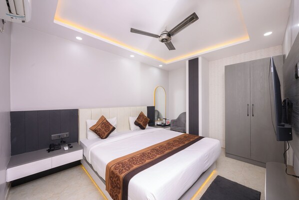A modern hotel room with a large bed, bedside tables, a ceiling fan, and a wardrobe. - Hotel Maharani Palace (varanasi)