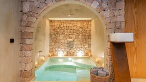 Ein Spa-Bereich mit Steinwänden, einer Whirlwanne, Kerzen und einem Korbwäscher mit Handtüchern.