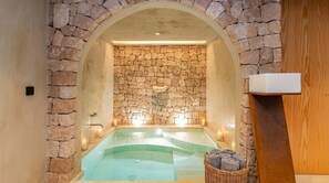 A stone-walled spa area with a hot tub, candles, and a wicker basket with towels. - Villa Can Nikita – Amazing Experience in Ibiza – Relax in Nature and Luxury (Ibiza)