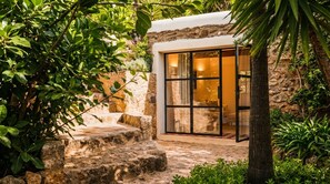 A stone-walled building with a glass door leading to an interior space. - Villa Can Nikita – Amazing Experience in Ibiza – Relax in Nature and Luxury (Ibiza)
