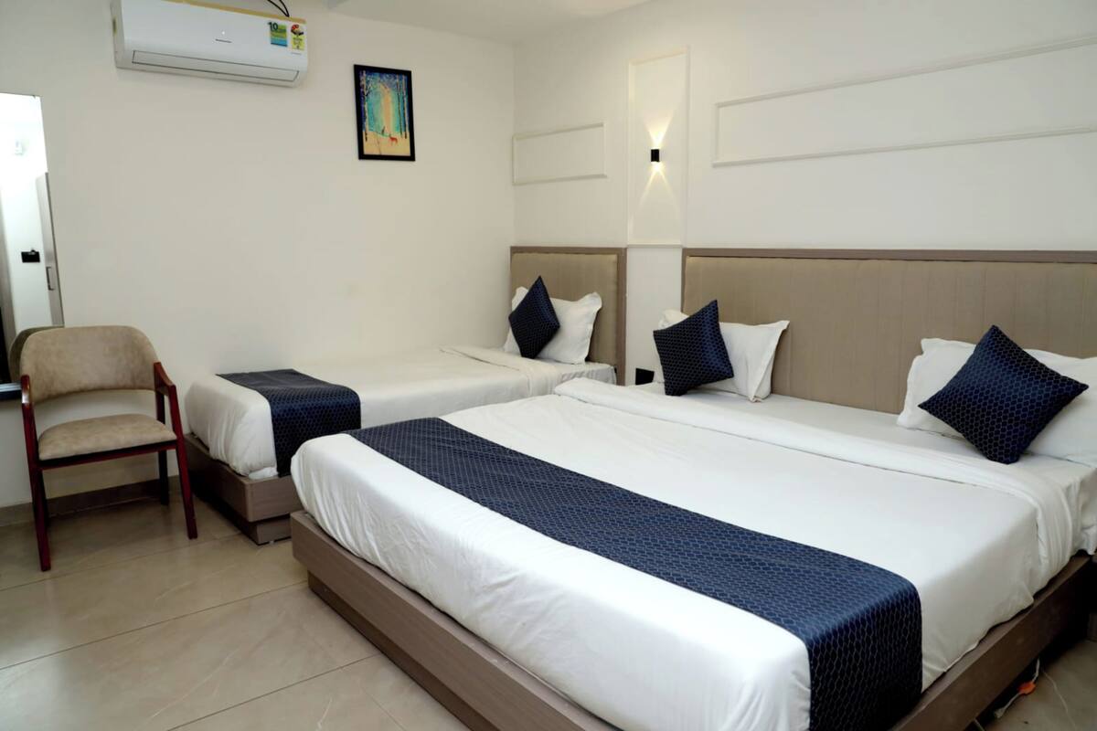 A hotel room with two single beds, a chair, a desk, and an air conditioning unit.