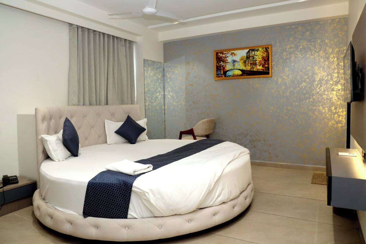 A well-appointed bedroom with a large bed, a ceiling fan, a painting on the wall, and a television on a stand.