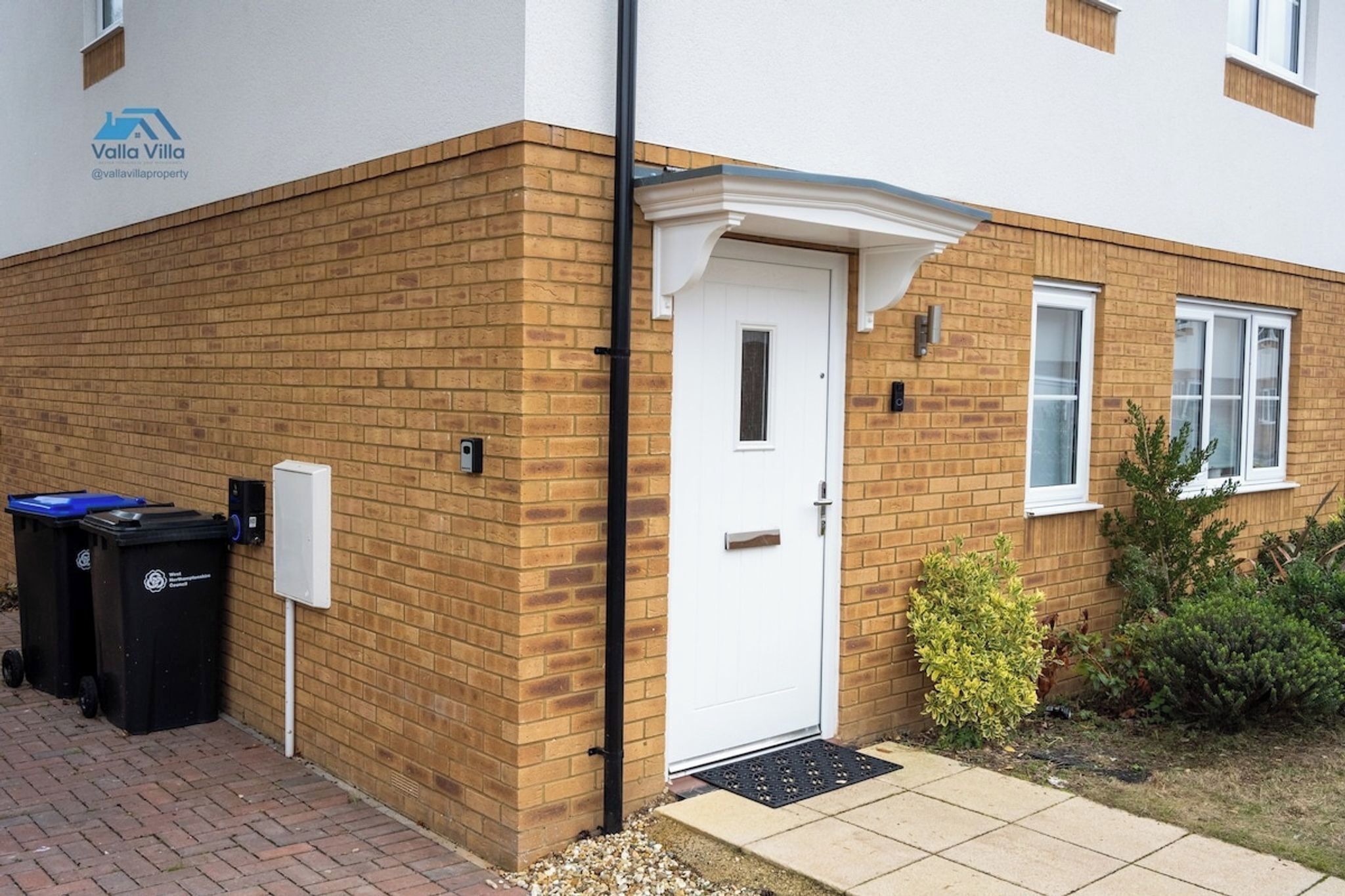 A residential building with a white door, brick walls, and a small garden.