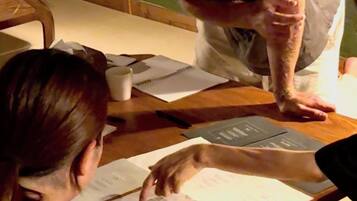 A person seated at a wooden table with papers, a cup, and a notebook.