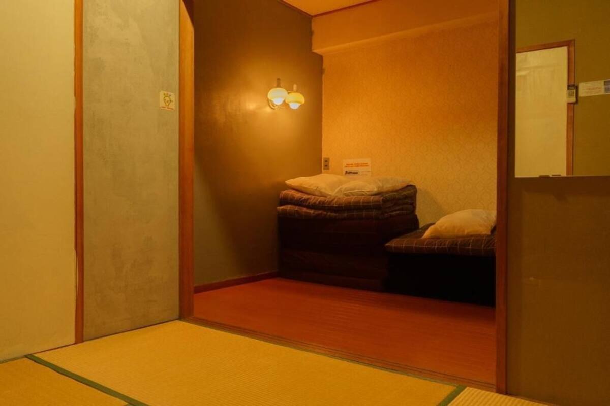 Una habitación pequeña, con poca luz, que tiene una cama individual, una lámpara de pared y un espejo.