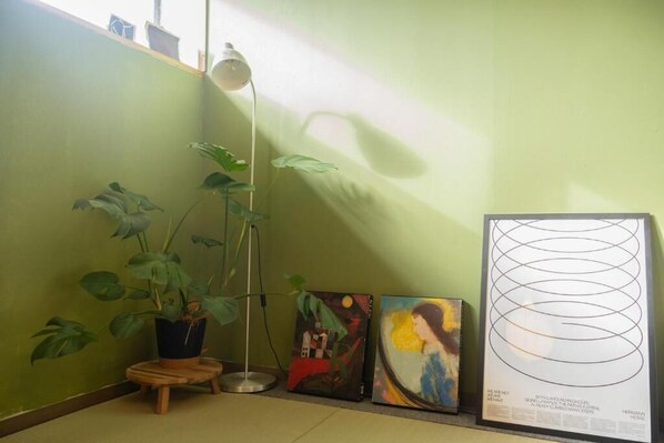Una habitación con pared verde, una lámpara de pie, una planta en maceta y tres obras de arte.