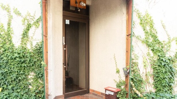 Un petit espace d’entrée fermé, doté d’une porte et entouré de verdure.