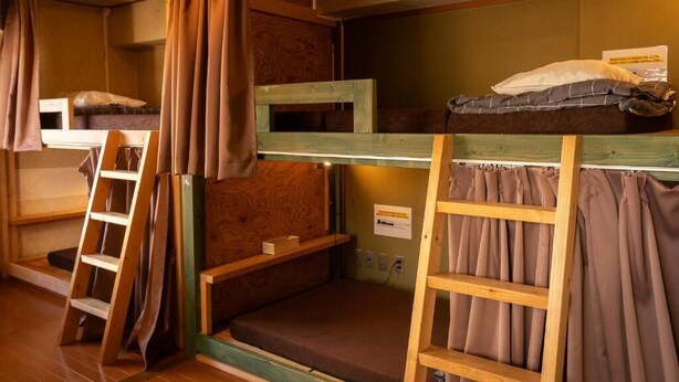 Ein Schlafsaalzimmer mit Stockbetten, Holzleitern und Vorhängen.