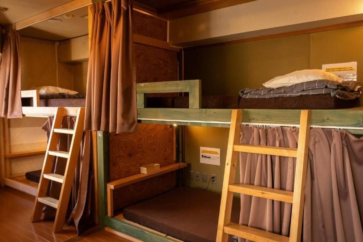 Un dormitorio tipo residencia con literas, escaleras de madera y cortinas.